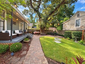 A backyard with a paved patio, outdoor seating, and a well-maintained lawn. - Downtown Secluded Cottage #4 (Pensacola)