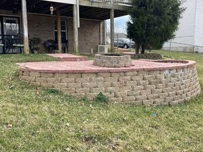 A circular stone fire pit with a brick border, surrounded by grass, in a residential outdoor area. - Modern stay-near Fort Knox (Radcliff)