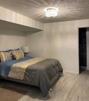 A bedroom with a bed, a nightstand, a lamp, and a door leading to another room. - Modern stay-near Fort Knox (Radcliff)