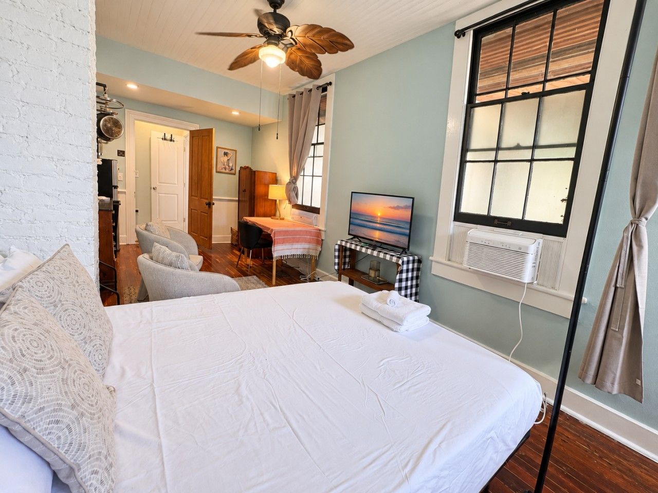 A bedroom with a large bed, a ceiling fan, a television, and a window with blinds.