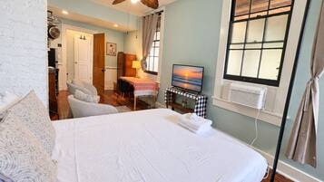 A bedroom with a large bed, a ceiling fan, a television, and a window with blinds.