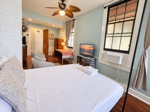 Een slaapkamer met een groot bed, een plafondventilator, een televisie en een raam met zonwering.