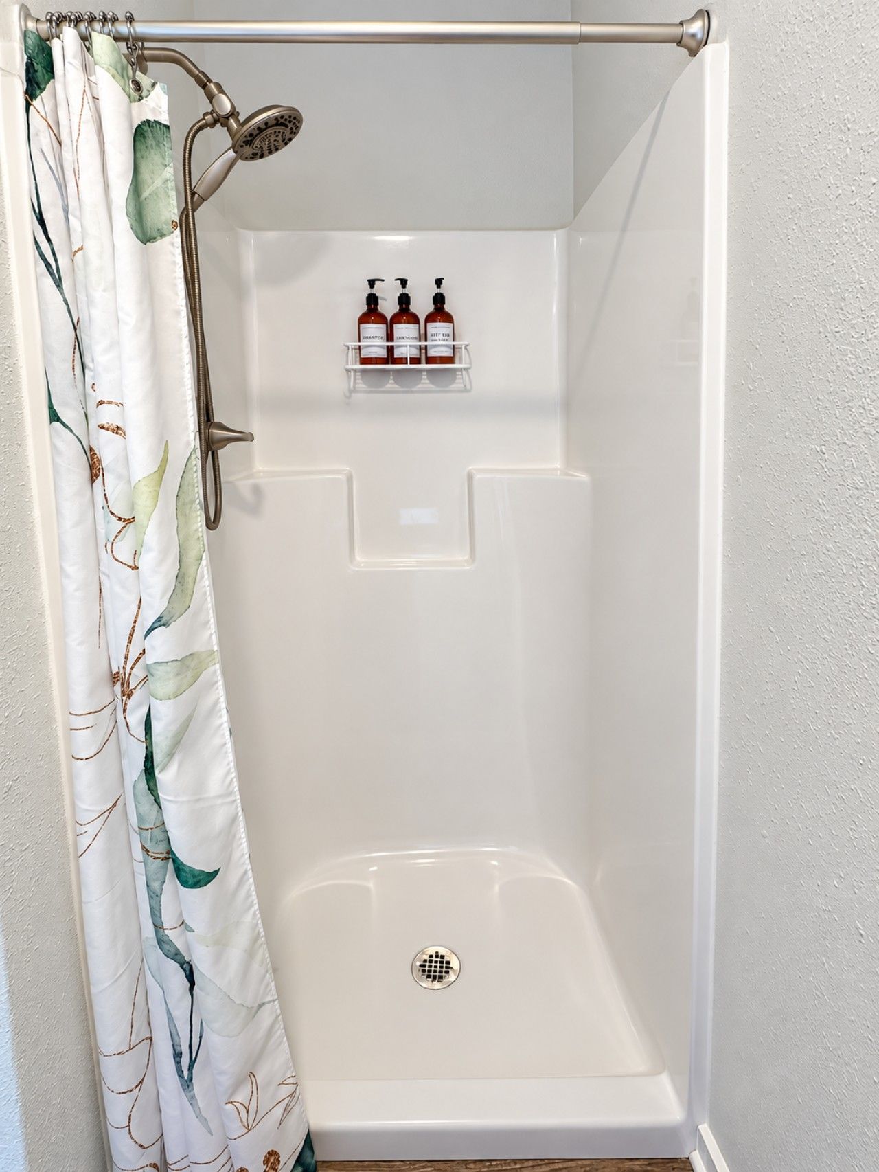 A shower area with a shower curtain, a showerhead, and a shelf with three bottles.
