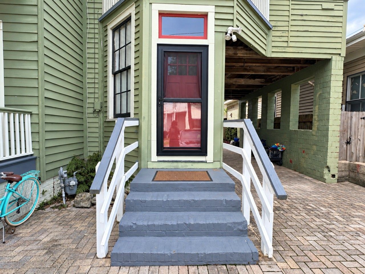 A green building with a red door, white railings, and a blue bicycle.