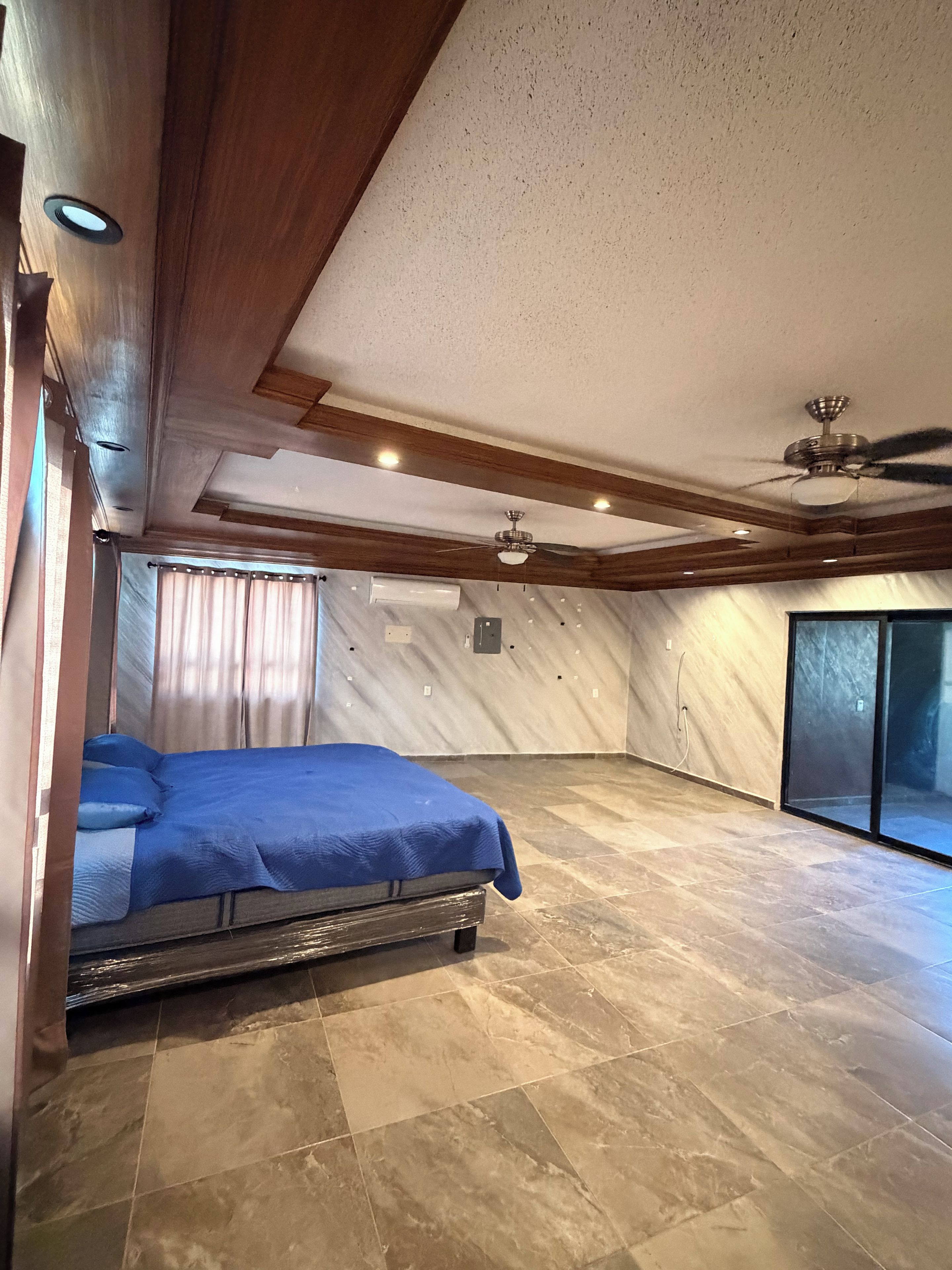Un dormitorio con cama, ventilador de techo y ventana grande.
