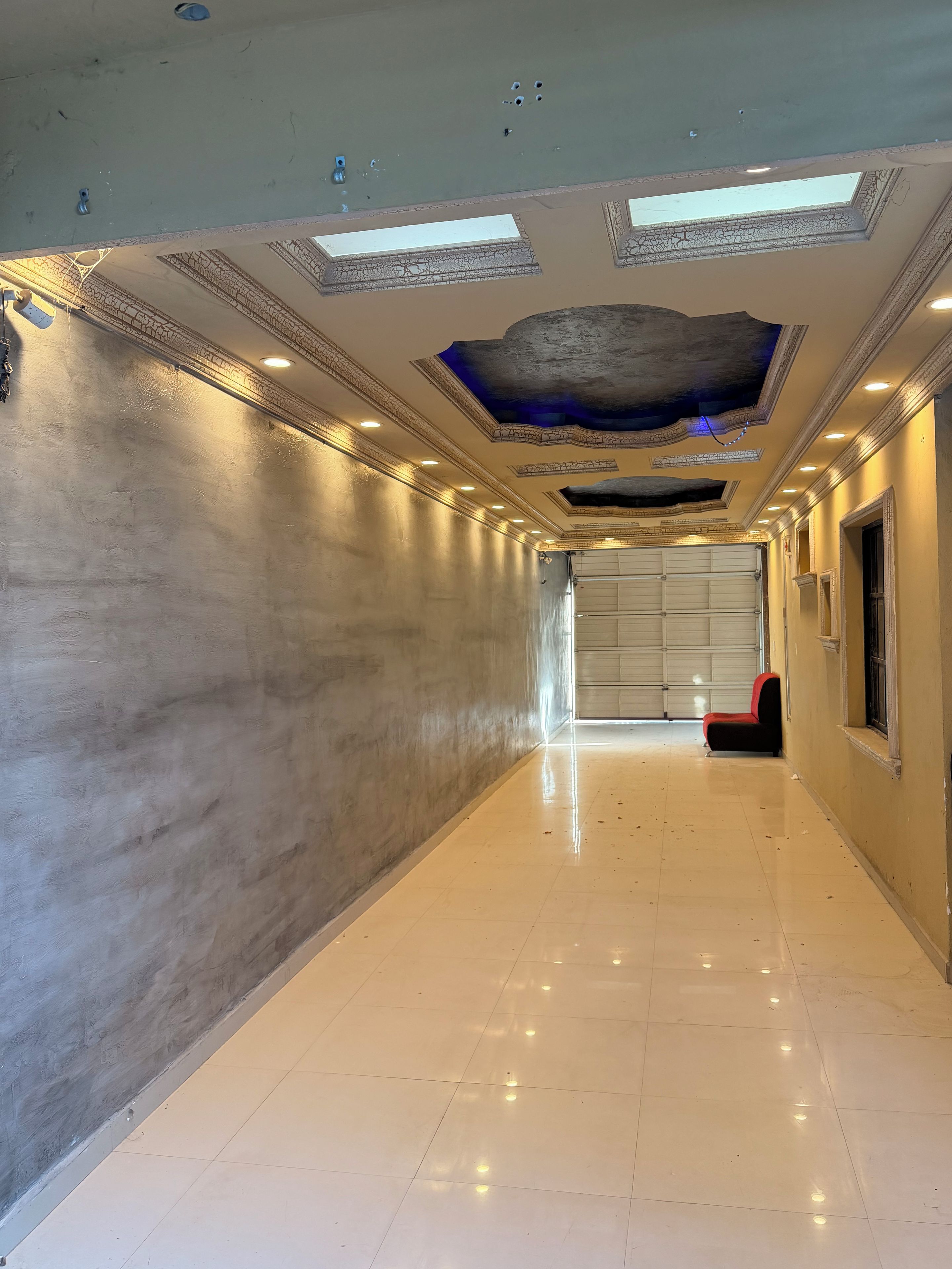 A corridor with a tiled floor, a red chair, and a garage door at the end.