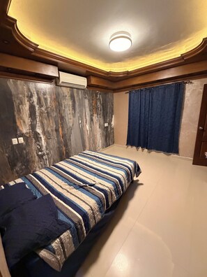 A room with a bed, a ceiling light, an air conditioning unit, and a curtain.