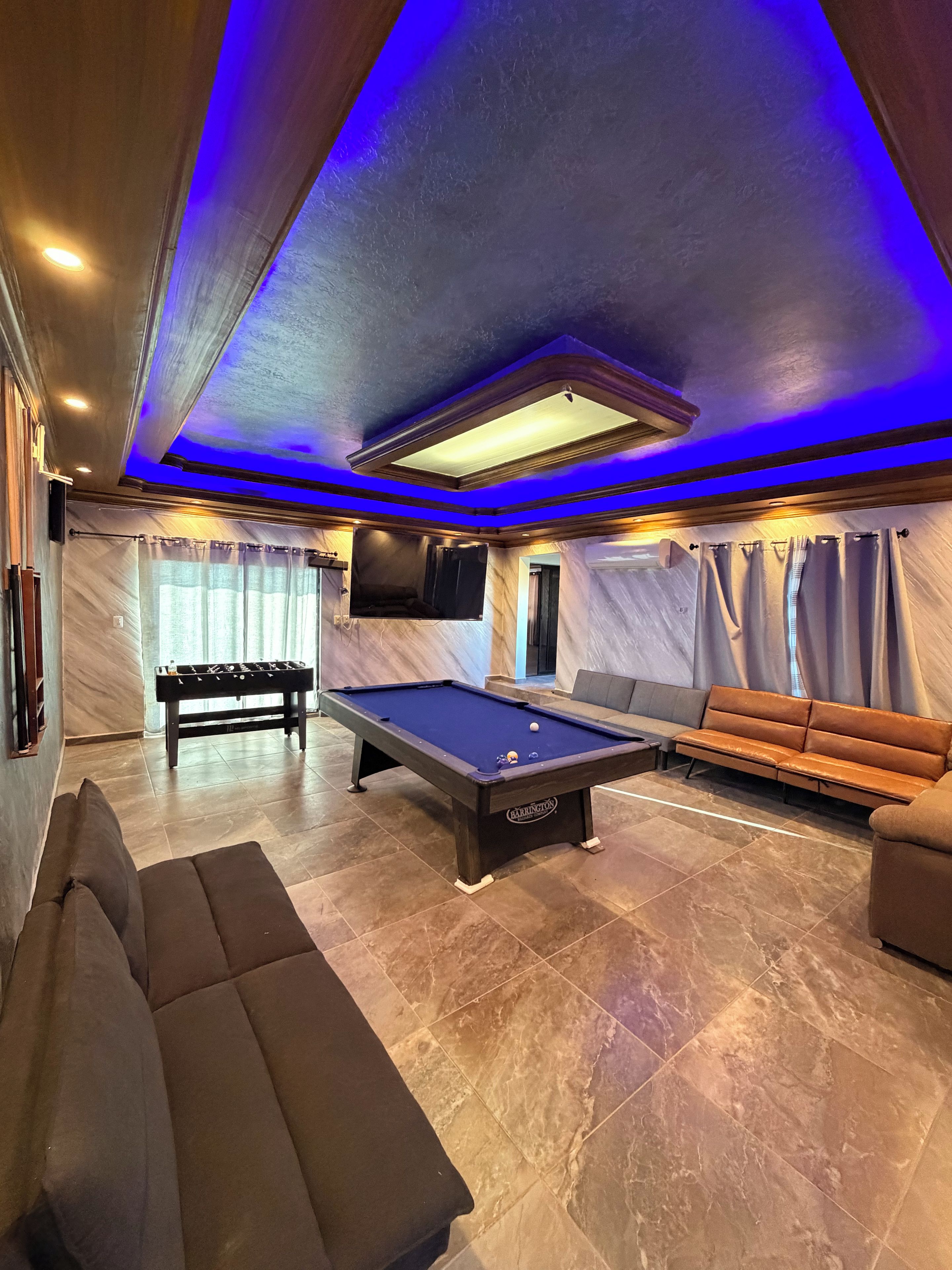 A pool table with a sofa and a billiards table in a room with a blue-lit ceiling.