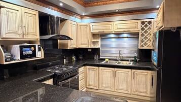 A kitchen with granite countertops, wooden cabinets, a stainless steel range hood, and a black refrigerator.