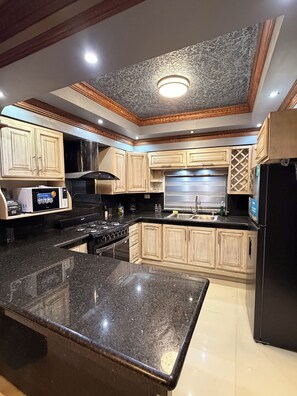 Una cocina con encimeras de granito, gabinetes de madera, campana extractora de acero inoxidable y un refrigerador negro.