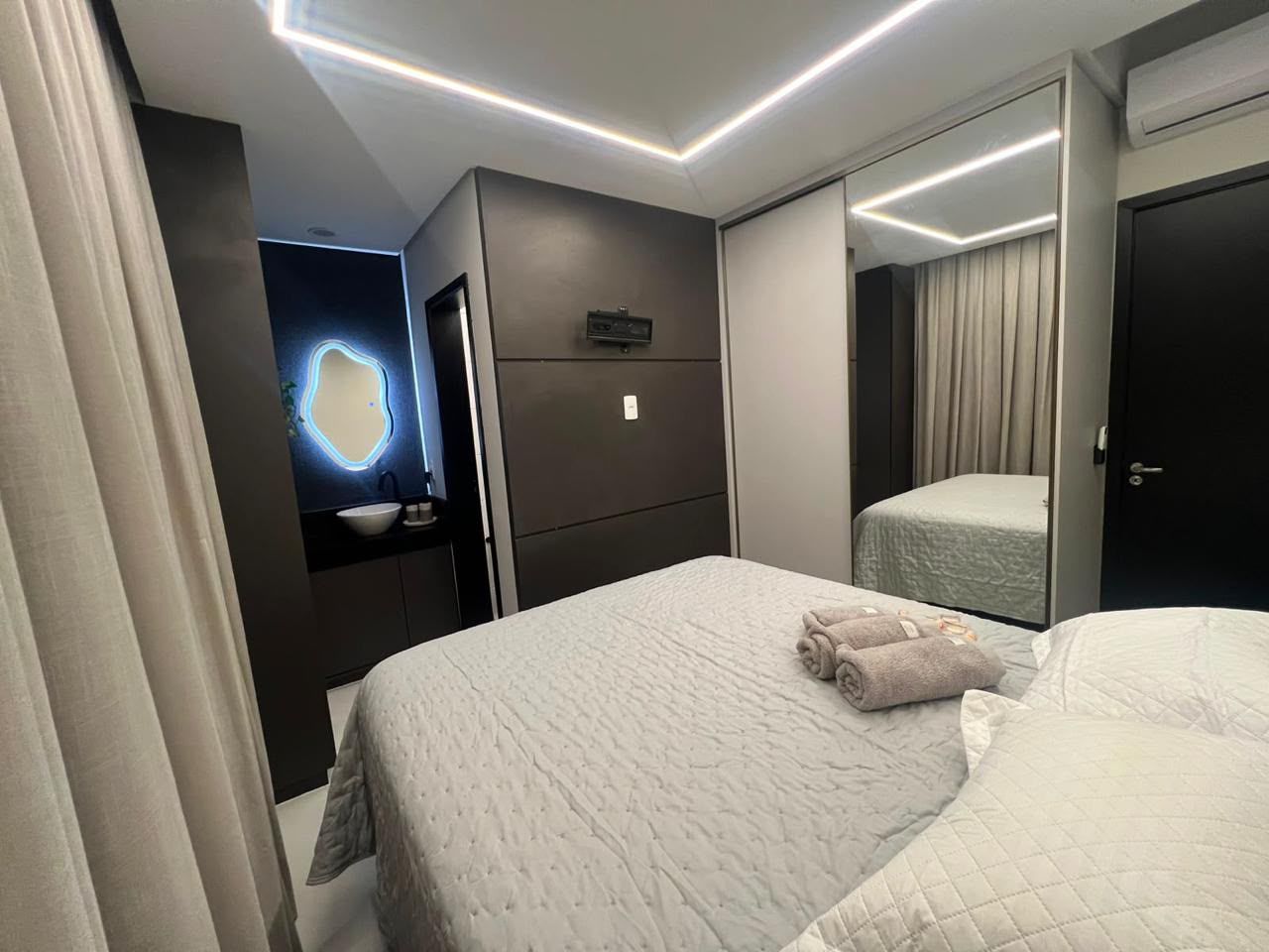 Una habitación de hotel con cama, mesita de noche, espejo y televisor montado en la pared.