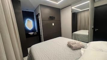 Una habitación de hotel con cama, mesita de noche, espejo y televisor montado en la pared.