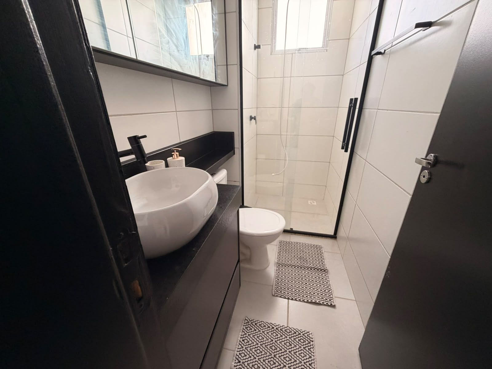 A compact bathroom with a white sink, toilet, and a glass shower enclosure.