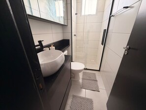 Un baño pequeño con lavamanos, inodoro y cabina de ducha de vidrio.