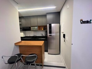 Cocina compacta con refrigerador integrado, microondas y pileta. Un pequeño mostrador de madera con dos sillas.