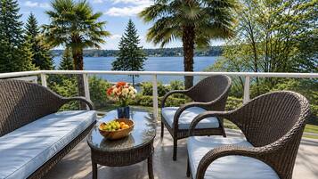 A balcony with wicker furniture, a glass table, and a bowl of fruit and flowers.