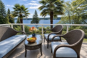 A balcony with wicker furniture, a glass table, and a bowl of fruit and flowers. - The Mercer Haven  (Mercer Island)
