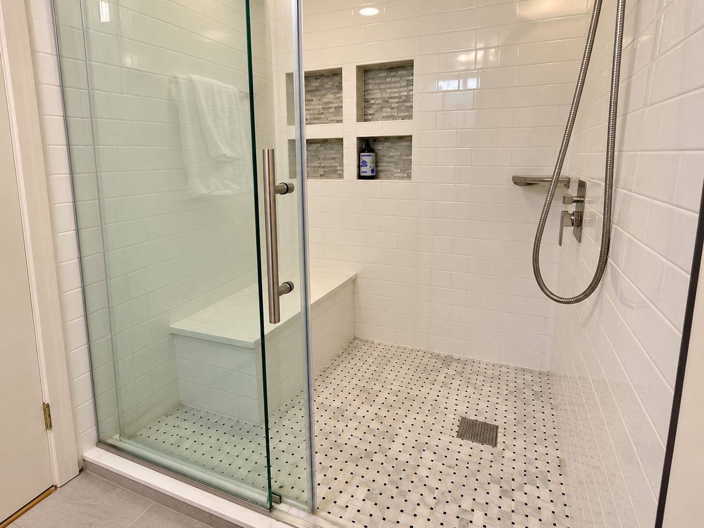 Un baño moderno con ducha envuelta en vidrio, paredes de azulejos blancos y un banco integrado.