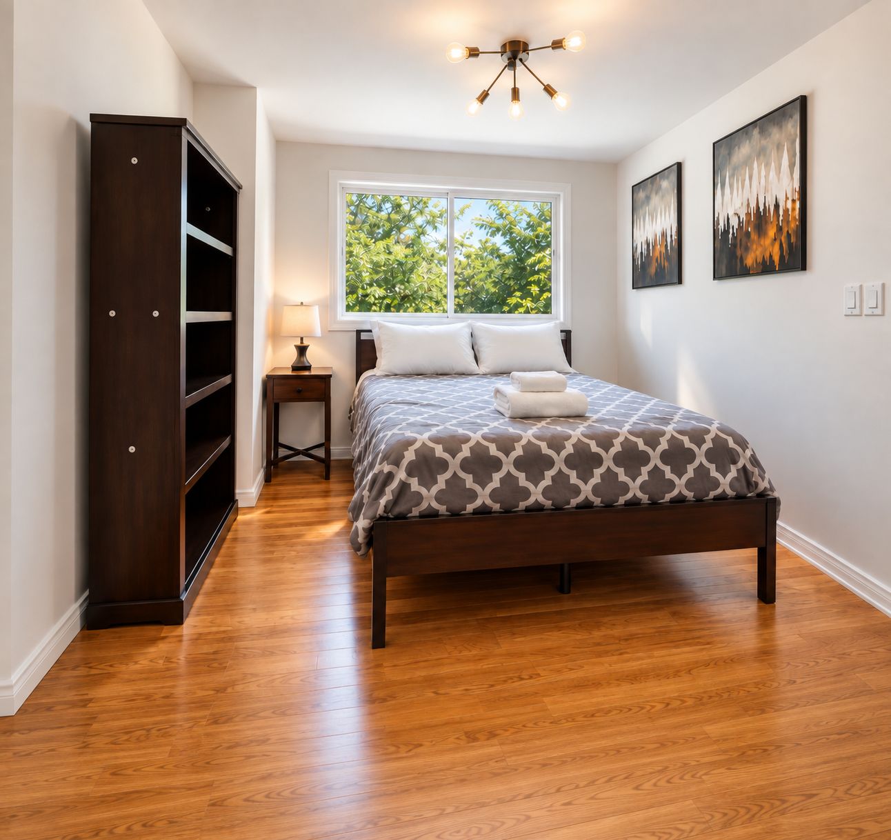 A bedroom with a bed, a wardrobe, a nightstand, a window, and artwork on the wall.