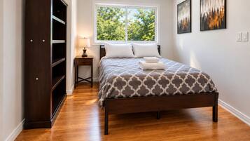 A bedroom with a bed, a wardrobe, a nightstand, a window, and artwork on the wall.