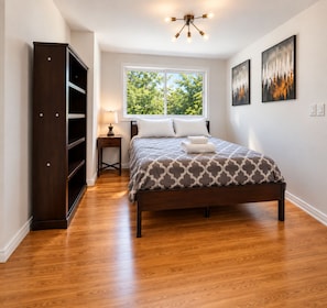A bedroom with a bed, a wardrobe, a nightstand, a window, and artwork on the wall. - The Mercer Haven  (Mercer Island)
