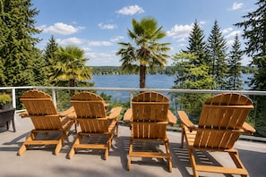 A deck with four wooden Adirondack chairs facing a lake, surrounded by trees and a clear sky. - The Mercer Haven  (Mercer Island)