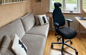 A room with a grey sofa, black office chair, and a window with a view of the outside. - Beautiful home in Fårösund with sauna (Fårösund)