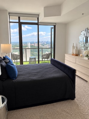 A modern bedroom with a large bed, a view of the city, and a balcony with outdoor furniture. - The Skyline Retreat @ Atlantic Station - Rooftop Pool & Gym (Atlanta)