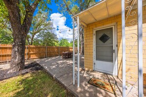 A covered patio with a wooden fence, a tree, and a door with decorative metalwork. - Violet Haus - 3 blocks from downtown (Fredericksburg)