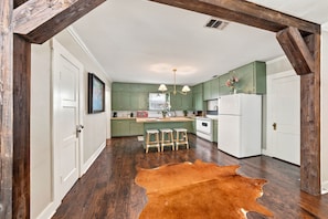 A kitchen with green cabinets, a white refrigerator, wooden stools, and a cowhide rug. - Violet Haus - 3 blocks from downtown (Fredericksburg)