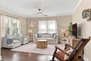 Ein Wohnzimmer mit einer Couch, gestreiften Stühlen, einem Couchtisch, einem Fernseher und einem Deckenventilator.