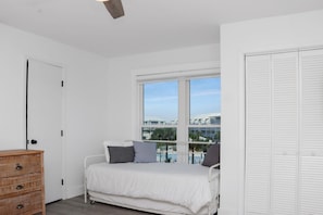 A bedroom with a bed, a dresser, and a view of a pool and buildings.