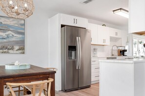 A modern kitchen with a stainless steel refrigerator, white cabinetry, and a wooden dining table.
