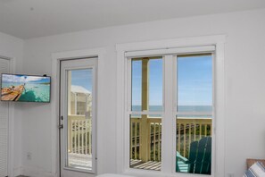 Een kamer met een schuifglazen deur die leidt naar een balkon met uitzicht op de oceaan.