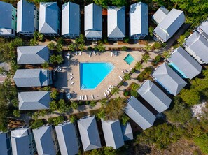 Vista aérea de un resort con varias edificaciones, una piscina central y palmeras circundantes.