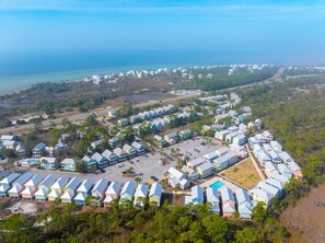An aerial view of a coastal residential area with multiple colorful houses, a parking lot, and a road leading to the beach. - Barefoot Cottage A3 (Port St. Joe)