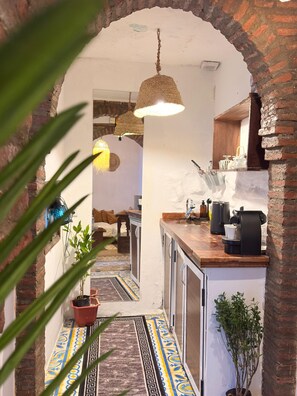 A narrow hallway with a tiled floor leading to a kitchen area with a coffee machine and a sink. - Dar Lala Khadouj (Chefchaouen)