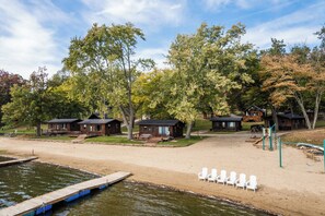 A lakeside cabin area with wooden structures, a dock, and beach chairs. - Dockside Sands at Sommer Dorf (West Branch)