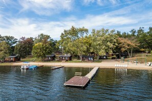 A lakeside cabin area with docked boats, wooden cabins, and a sandy beach. - Dockside Sands at Sommer Dorf (West Branch)