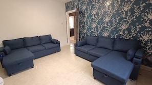 A living room with two sofas, a tiled floor, and a door leading to another room.