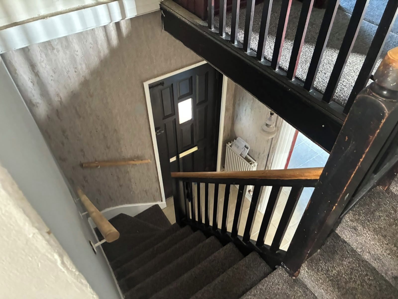 Una escalera con barandilla negra y pared blanca.