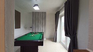 A pool table in a room with a window, curtains, and a ceiling light.