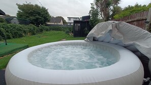 An inflatable hot tub with a cushion and a cover, surrounded by a grassy yard and a wooden fence.