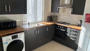 Cocina compacta con lavadora, microondas, fregadero, estufa y alacenas.