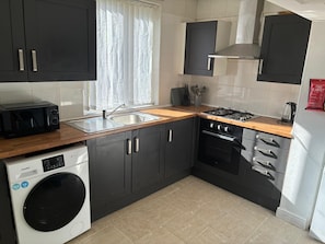 Cocina compacta con lavadora, microondas, fregadero, estufa y alacenas.