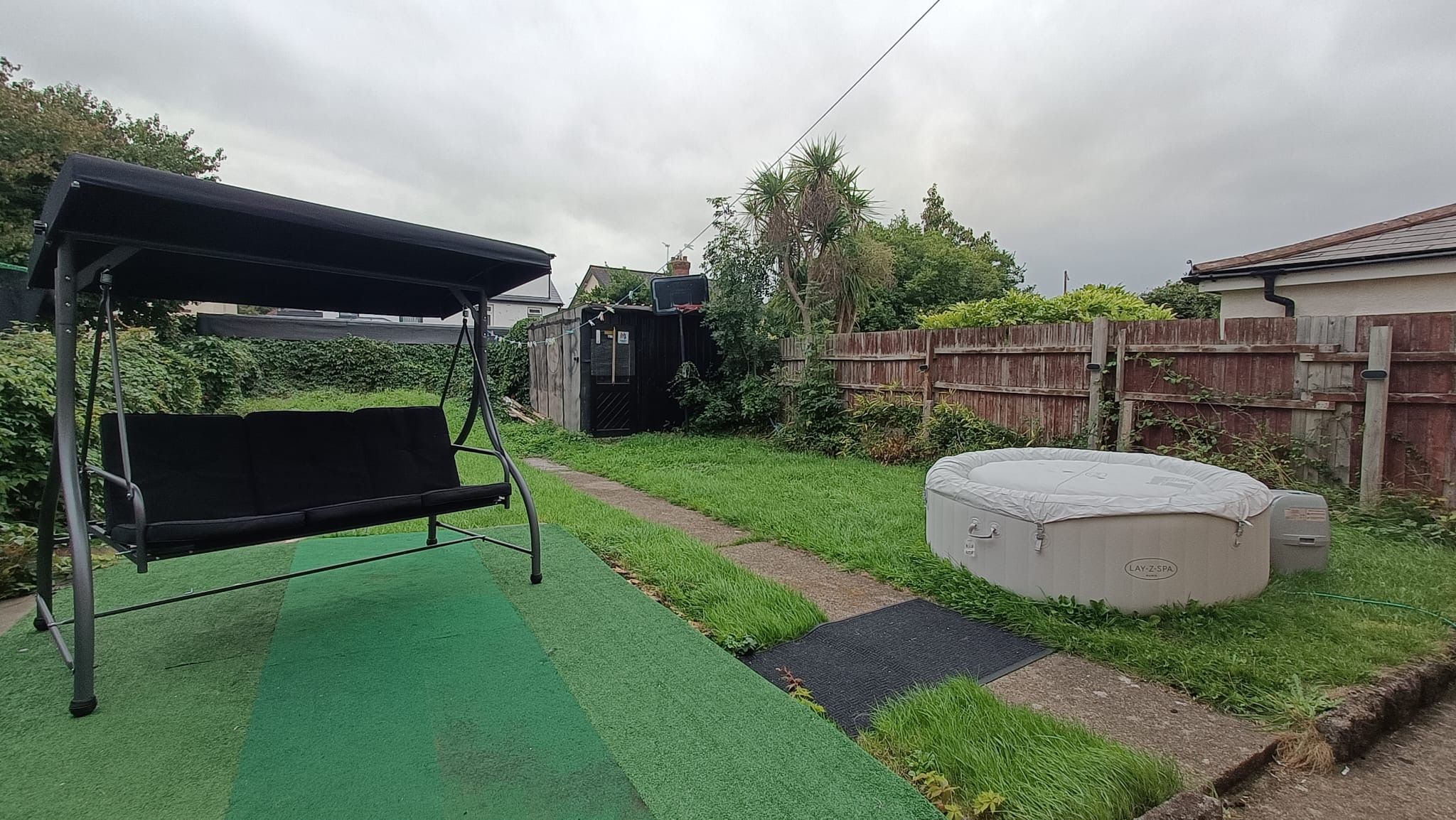Un patio trasero con un columpio, un jacuzzi y una zona delimitada por una cerca.