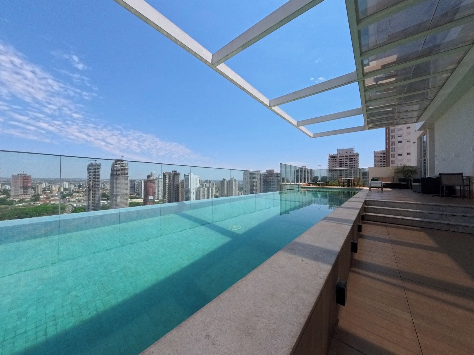 A rooftop infinity pool with a city view, surrounded by glass railings and modern outdoor furniture.