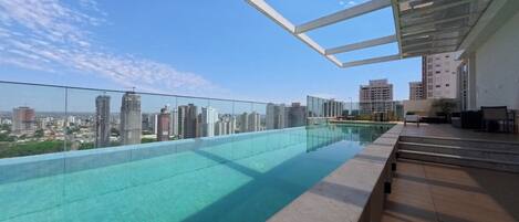 A rooftop infinity pool with a city view, surrounded by glass railings and modern outdoor furniture.