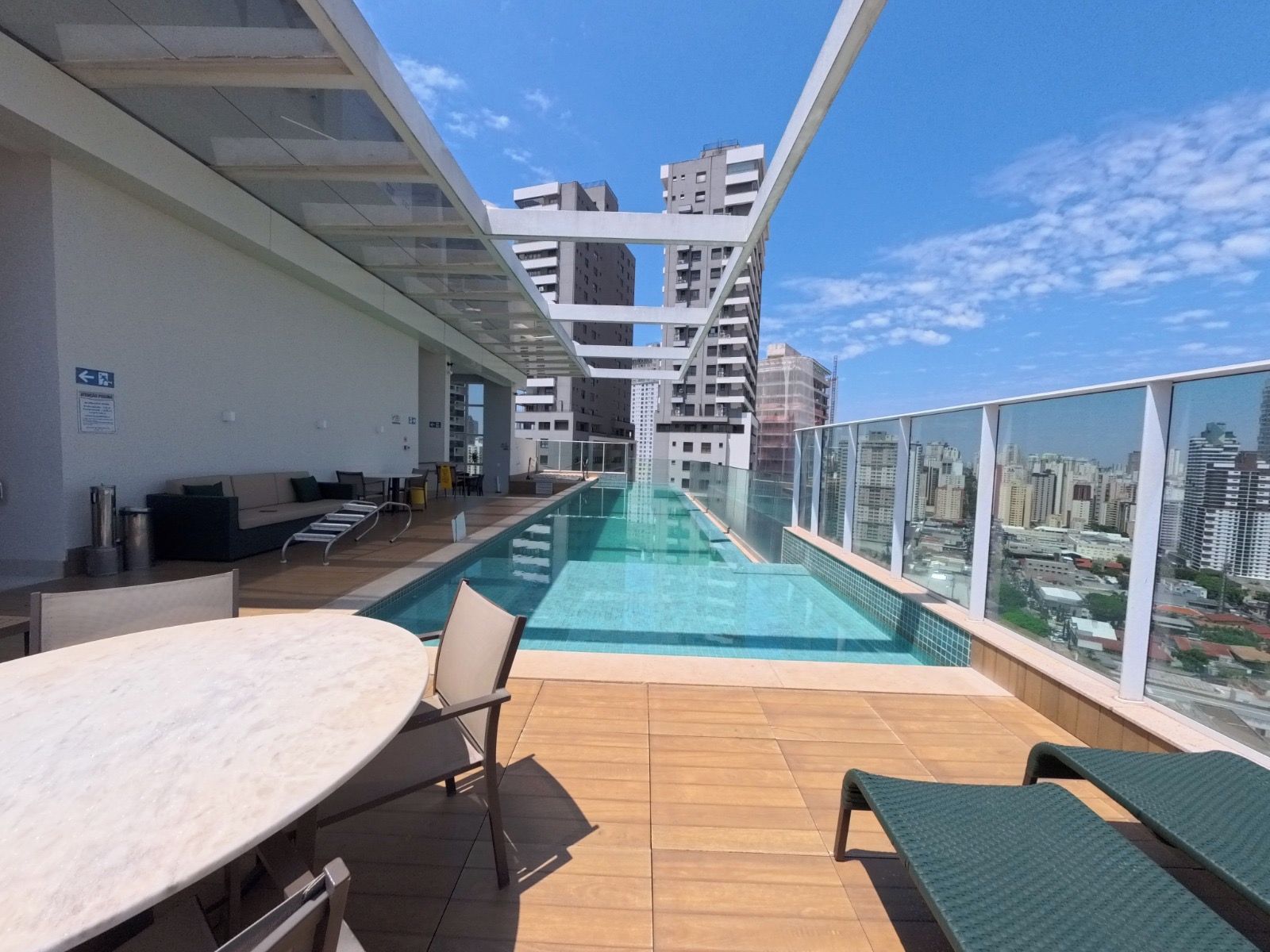 Un espace piscine aménagé sur le toit, doté d’une barrière en verre, de chaises longues et d’une table.