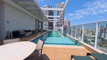 Un espace piscine aménagé sur le toit, doté d’une barrière en verre, de chaises longues et d’une table.